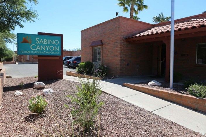 A brick building with a sign that reads 'Sabino Canyon' surrounded by desert landscaping under a clear blue sky.