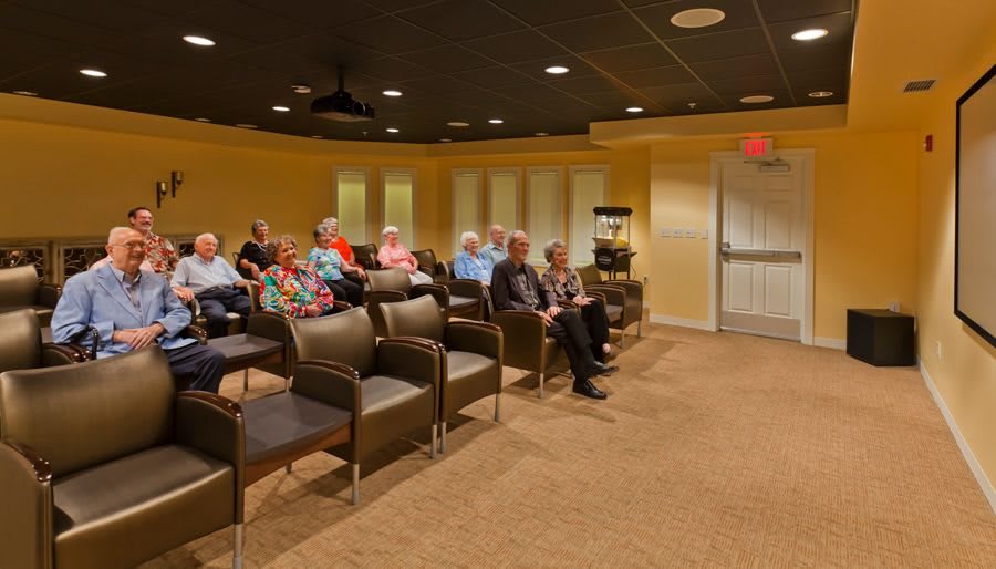 A small group of people seated in a conference room with rows of empty chairs.