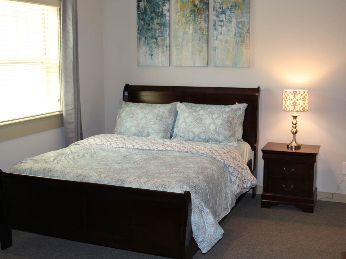 A cozy bedroom with a neatly made bed, nightstand and lamp, adorned with artwork above the headboard.