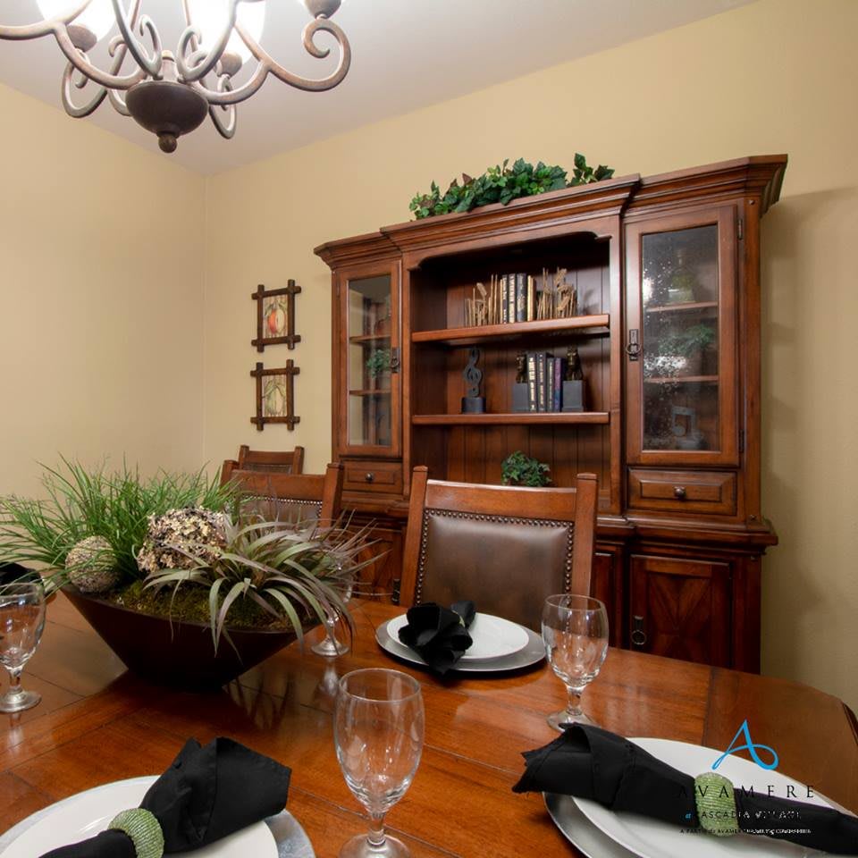 A cozy dining room featuring a wooden dining table set with glassware and napkins, complemented by a china cabinet and decorative plants.