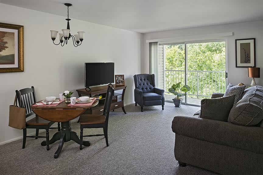 A cozy living room with a dining area, featuring a television, sofa, and large window overlooking greenery.