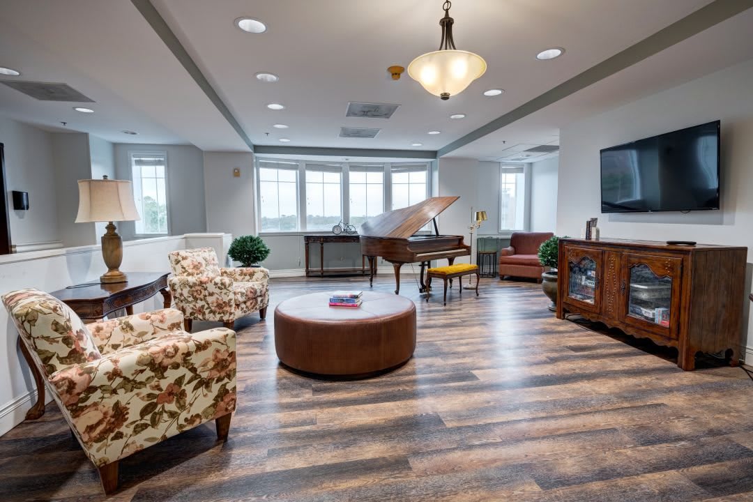 A spacious living room with a grand piano, cozy armchairs, and wooden flooring.