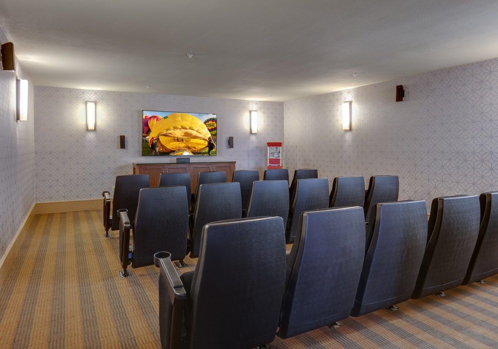 A cozy home theater room with rows of comfortable seats facing a projector screen.