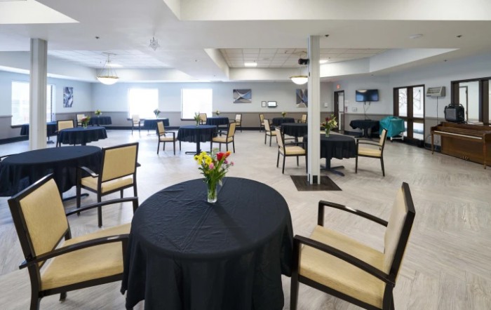 A spacious dining area with tables covered in black tablecloths, adorned with a vase of flowers.