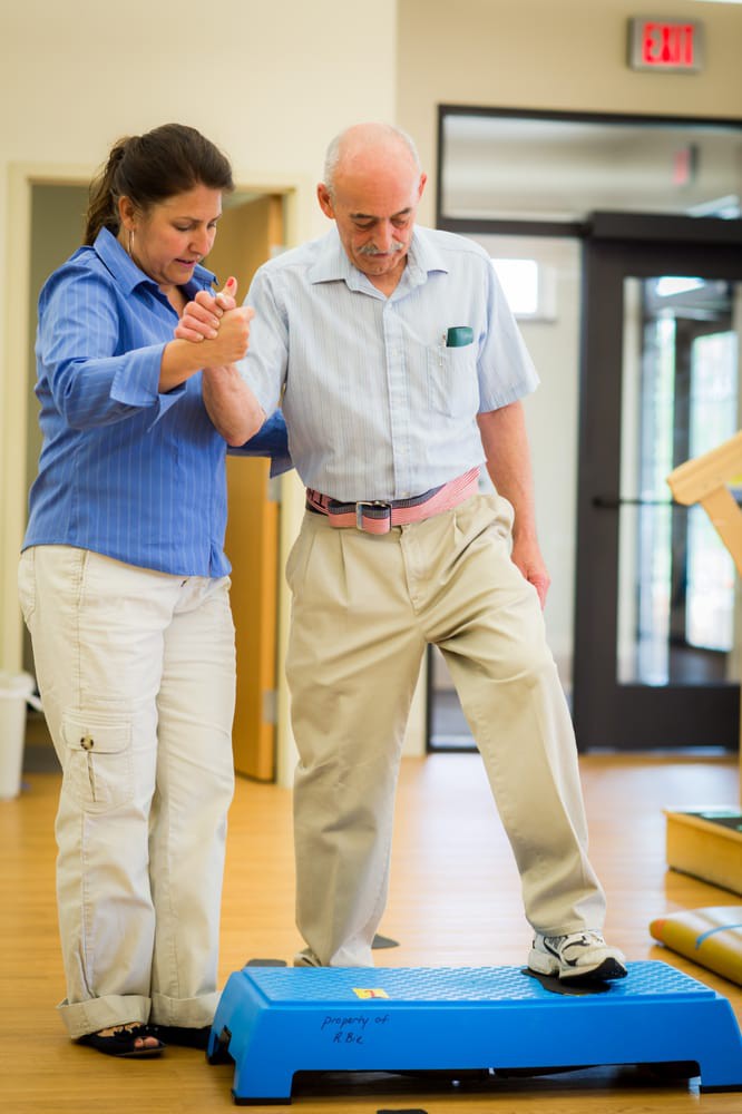A therapist assists an elderly man with physical rehabilitation exercises.