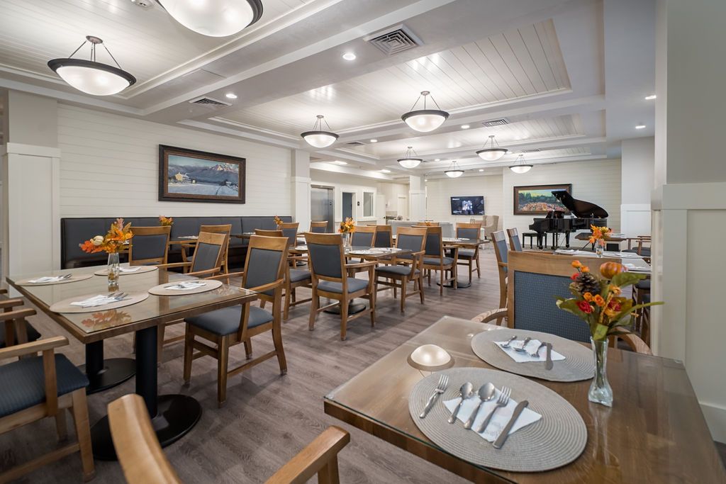A modern and elegantly designed restaurant dining area with neatly arranged tables and chairs, featuring chandelier lighting and a grand piano.
