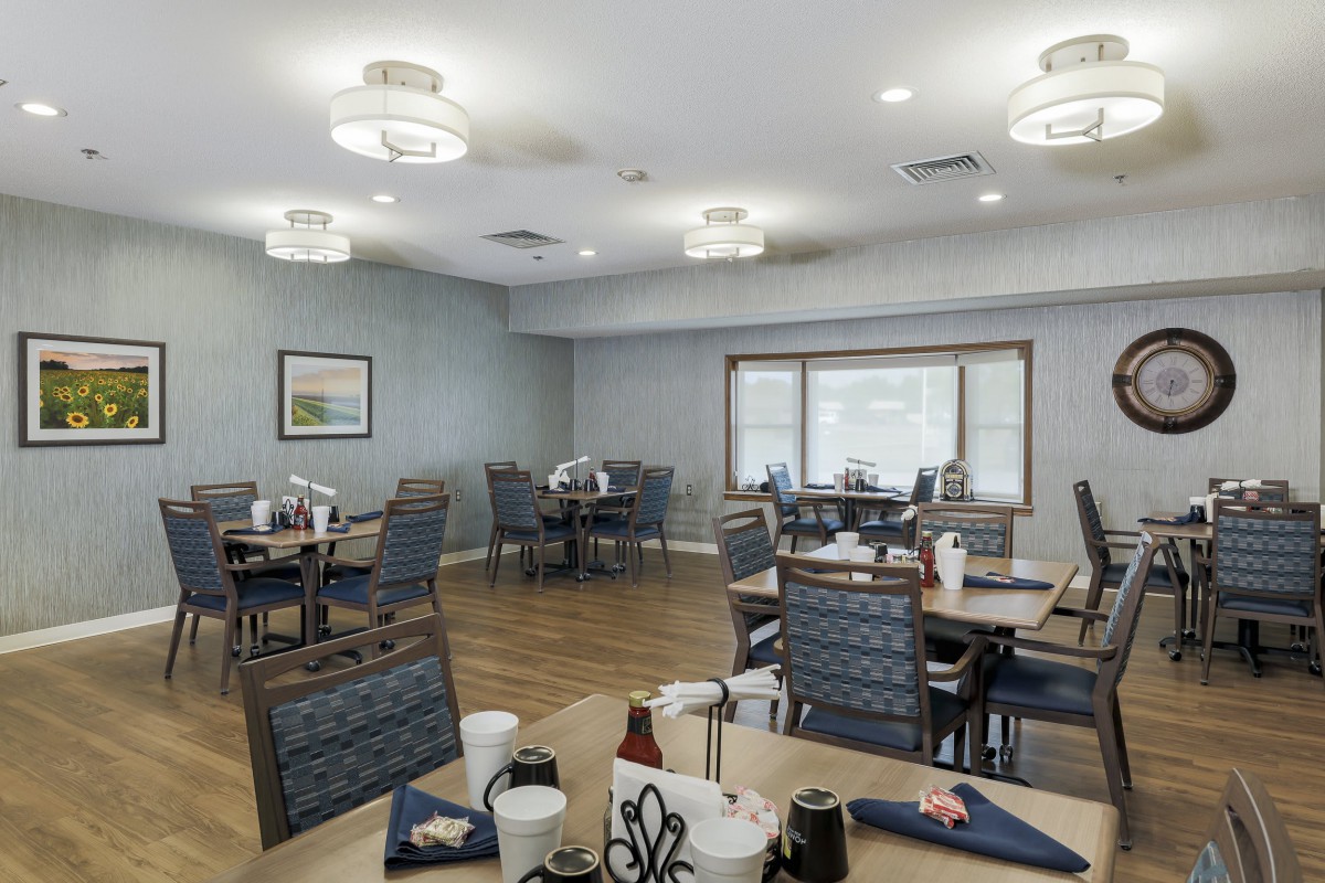 An empty dining room with neatly arranged tables and chairs, softly lit by ceiling lights.