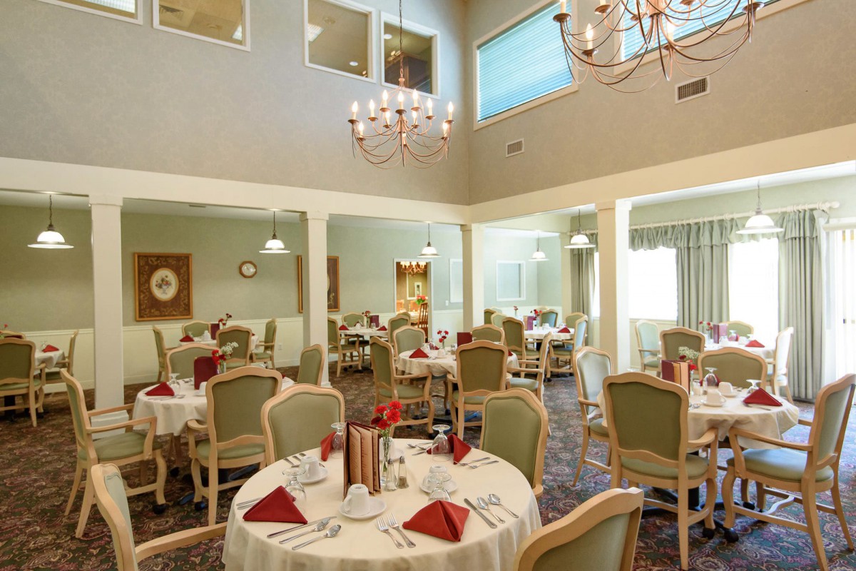An elegant dining room with neatly arranged tables, chandeliers, and large windows.