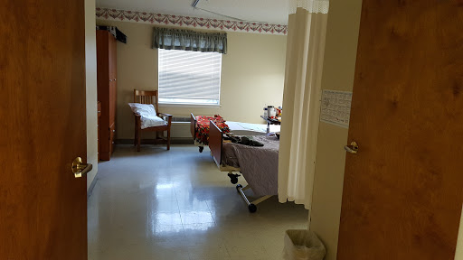 A view of a hospital patient room featuring a bed, seating area, and natural light from the window.