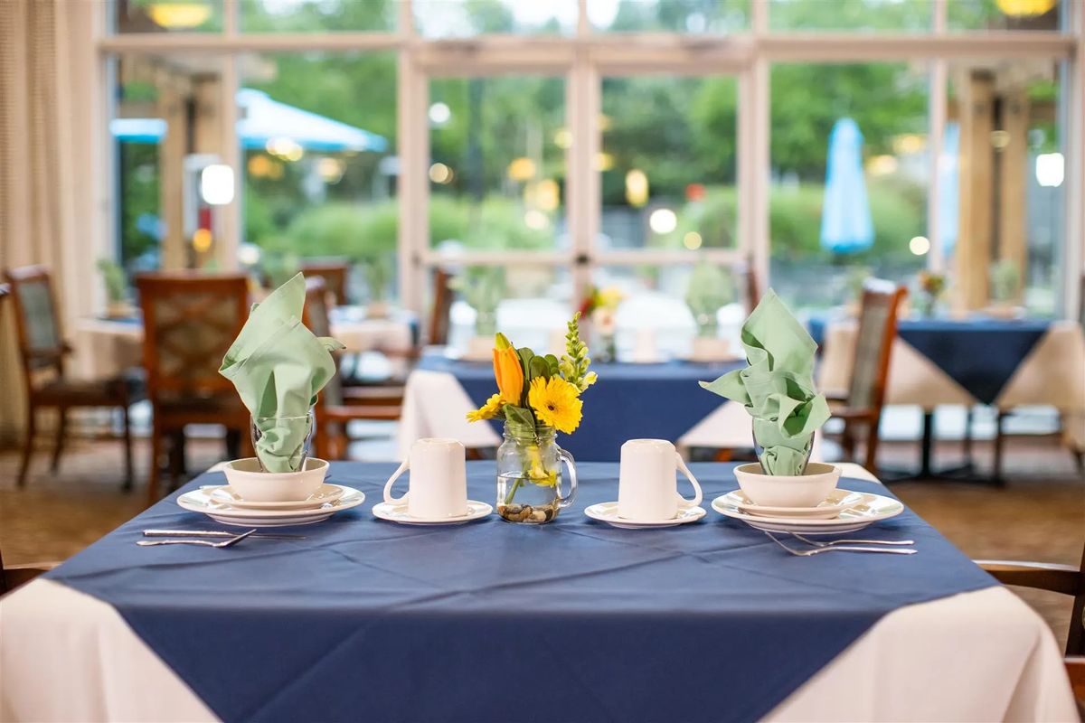 A beautifully set dining table with blue tablecloth, adorned with neatly folded napkins, cups, and a small floral centerpiece.