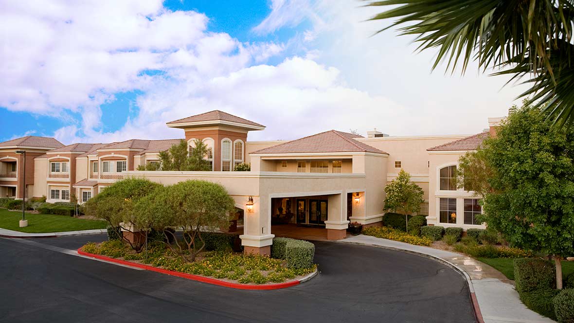 A modern hotel building with a landscaped entrance and a blue sky backdrop.