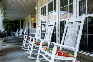 A row of white rocking chairs on a porch, creating a cozy outdoor seating area.