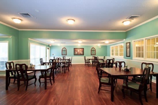 A spacious dining room with wooden floors, multiple tables and chairs, light-colored walls decorated with artwork.
