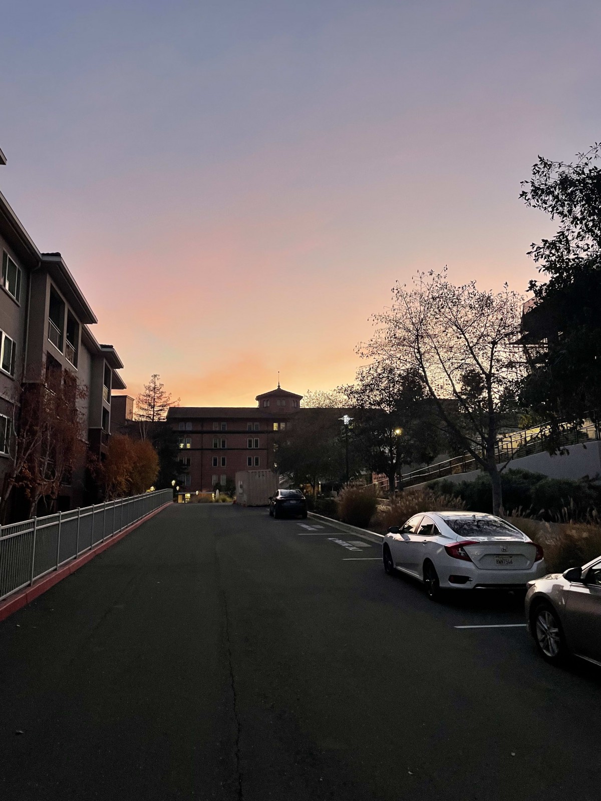A quiet street scene at sunset with cars parked along the road.
