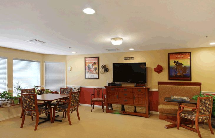 A cozy living room with a television, chairs, and a table, adorned with wall decorations.