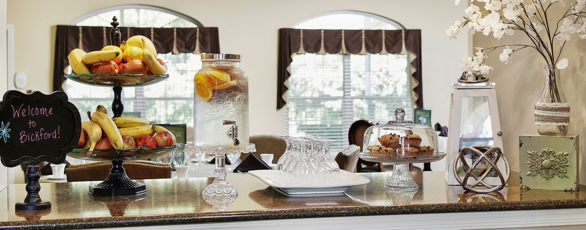 A kitchen countertop with a lemon water dispenser and a platter of cookies near a bright window.