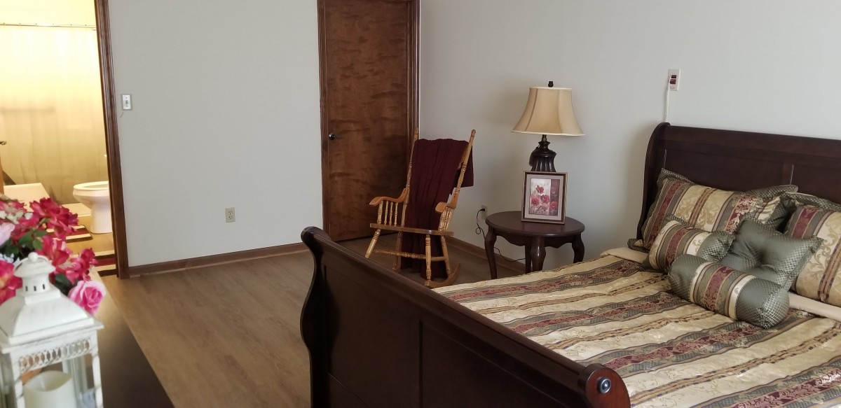 A cozy bedroom corner with a wooden rocking chair, side table, and lamp.
