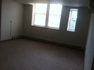 An empty room with carpet flooring and large windows letting in natural light.
