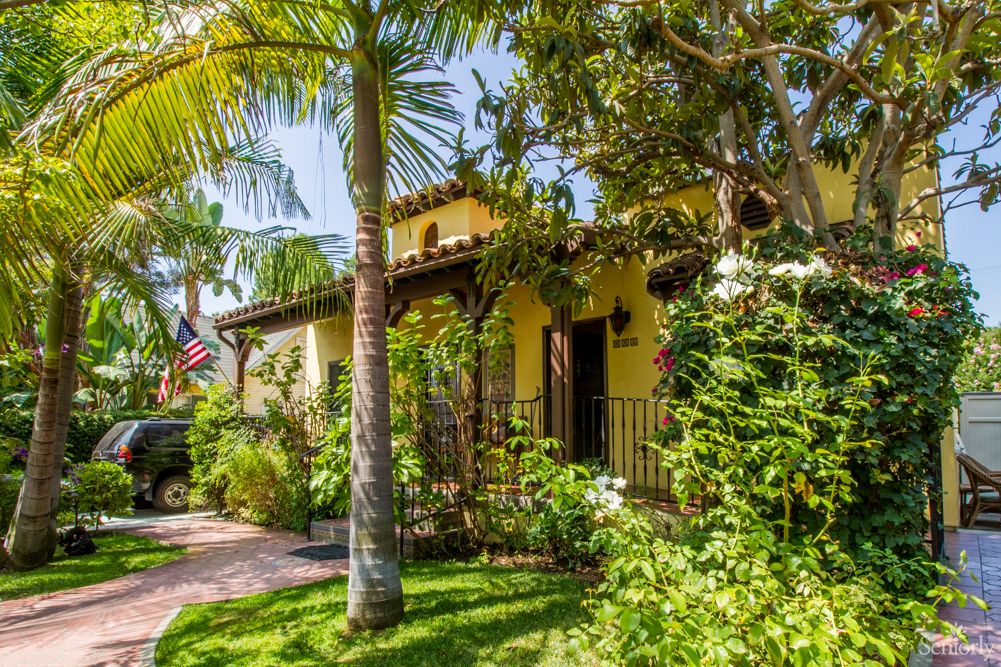 A charming house with a lush, tropical garden and palm trees on a sunny day.