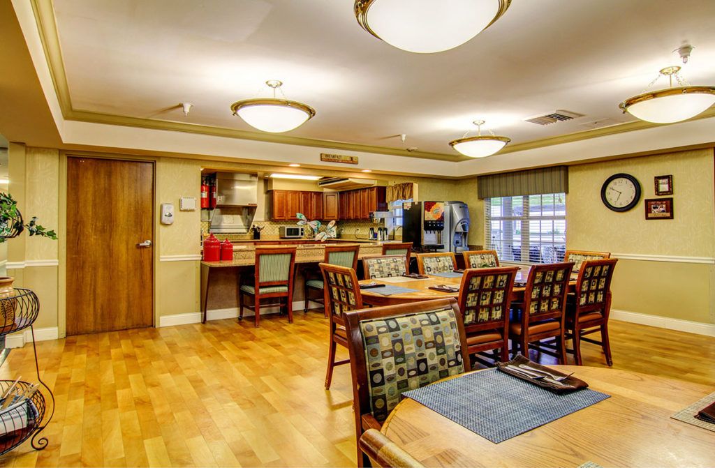A spacious and well-lit dining area with a kitchen, featuring wooden flooring and comfortable seating.