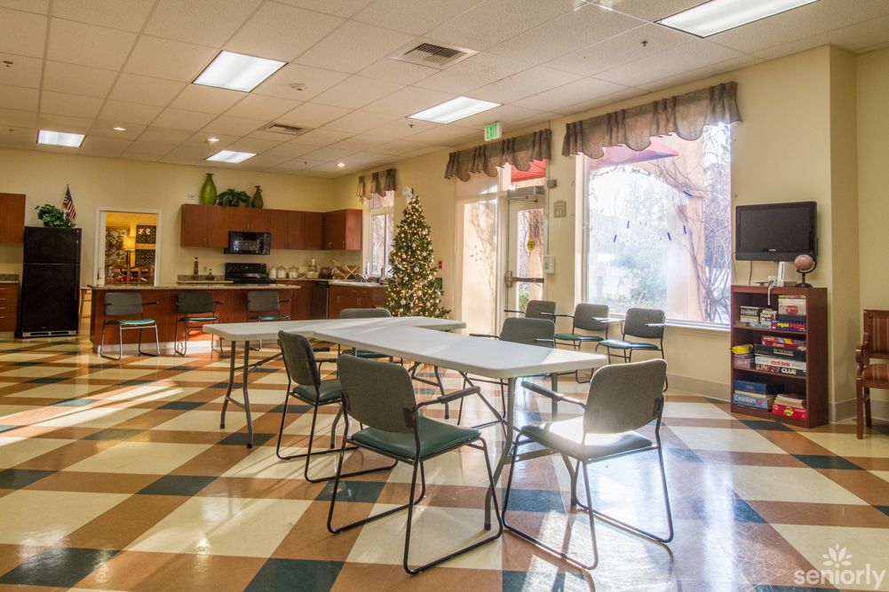 A well-lit multipurpose room with a decorated tree, featuring a table and chairs, and a kitchen area.