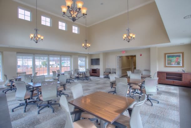 A spacious dining area with multiple tables and chairs, illuminated by chandeliers, featuring large windows and a neutral color scheme.
