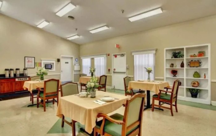 A well-lit dining area with tables and chairs arranged neatly, featuring simple decor and large windows.