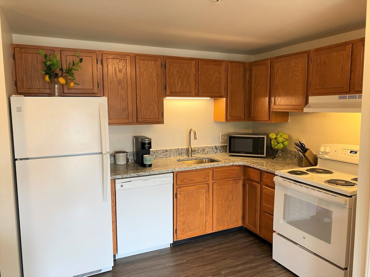 A cozy kitchen featuring wooden cabinets, a white refrigerator, dishwasher, microwave, and a coffee maker.