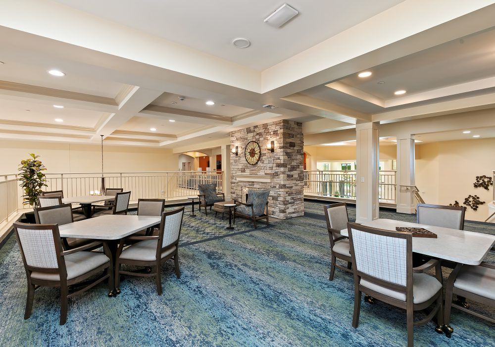 A spacious and well-lit dining area with neatly arranged tables and chairs, featuring a stone wall accent and blue carpeting.