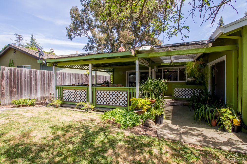 A charming backyard view of a house with a covered patio surrounded by greenery.