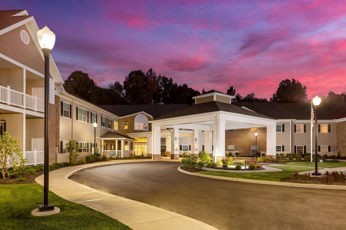A beautifully lit building exterior at sunset with a curved driveway and landscaped surroundings.