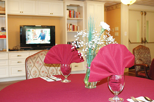A beautifully set dining table with red napkins and decorative flowers, complemented by a television in the background.