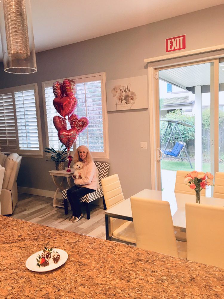 A person sitting in a decorated room with heart-shaped balloons and a dining area.