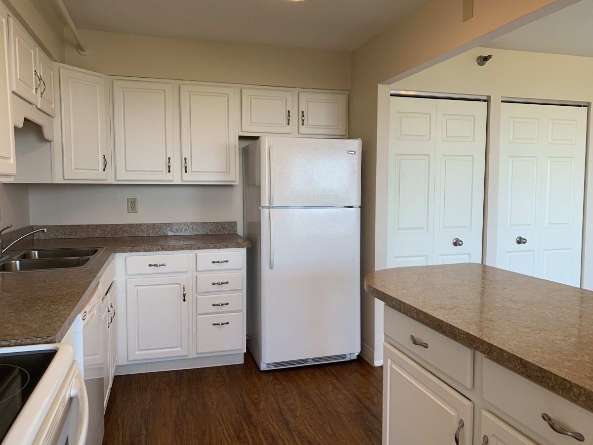 A kitchen with white cabinets, a refrigerator, and wooden flooring.