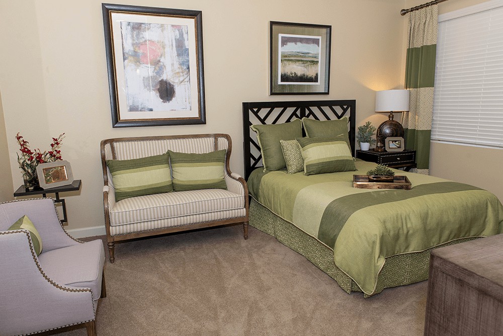 A cozy bedroom with green bedding and framed artwork on the walls.