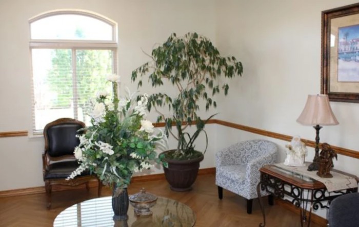 A cozy living room corner with a large indoor plant, a comfortable chair, and a table adorned with a floral arrangement.