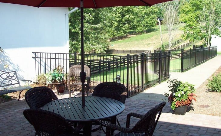 A cozy patio with a table and chairs under an umbrella, overlooking a garden and fenced yard.