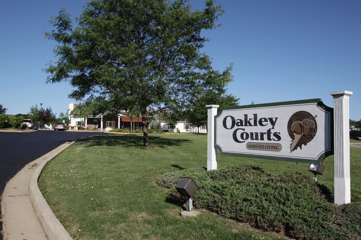 Entrance sign for Oakley Courts with lush greenery and buildings in the background.