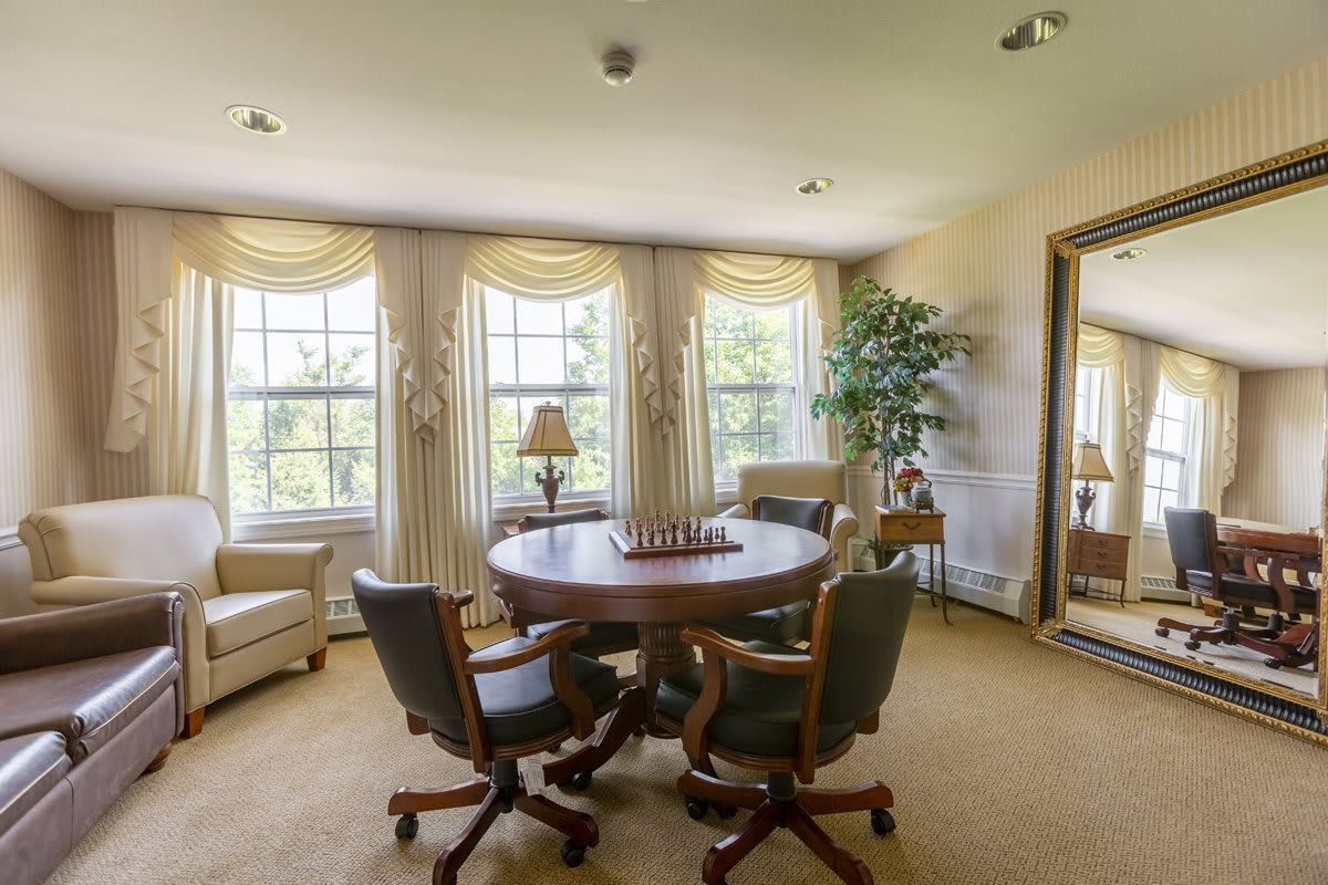 A cozy sitting area with a round table set for chess, surrounded by comfortable chairs and large windows with elegant curtains.