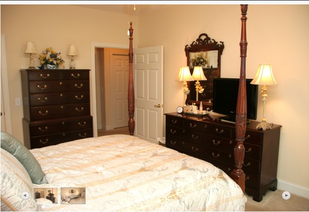 A cozy bedroom featuring a four-poster bed, dresser with mirror, and bedside lamps.
