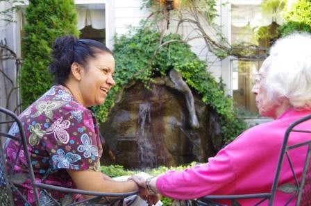 A caregiver and an elderly person enjoying a conversation in a garden setting.