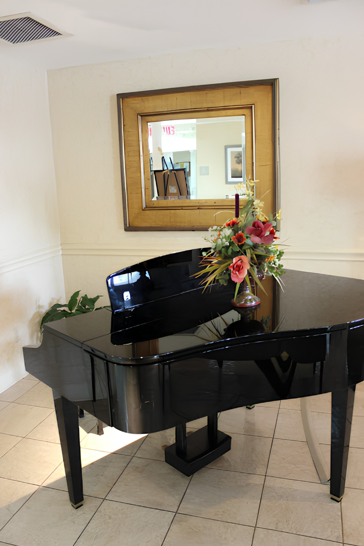 A grand piano adorned with a floral arrangement, positioned in front of a wall mirror.