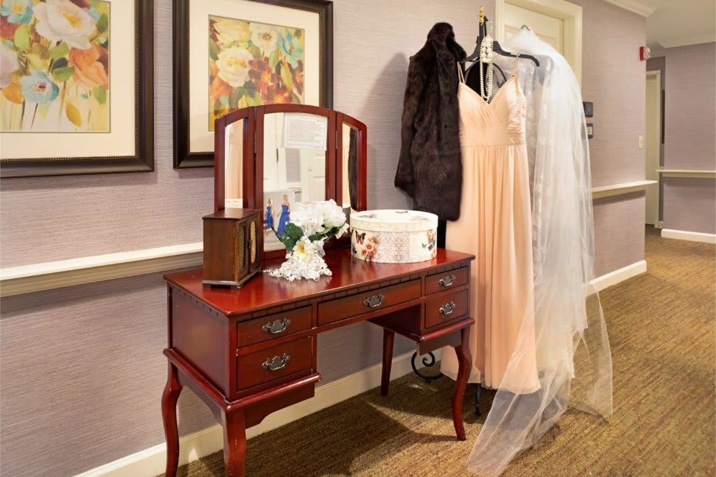 A dressing table adorned with a mirror, flowers, and a wedding dress with a veil hung beside it.