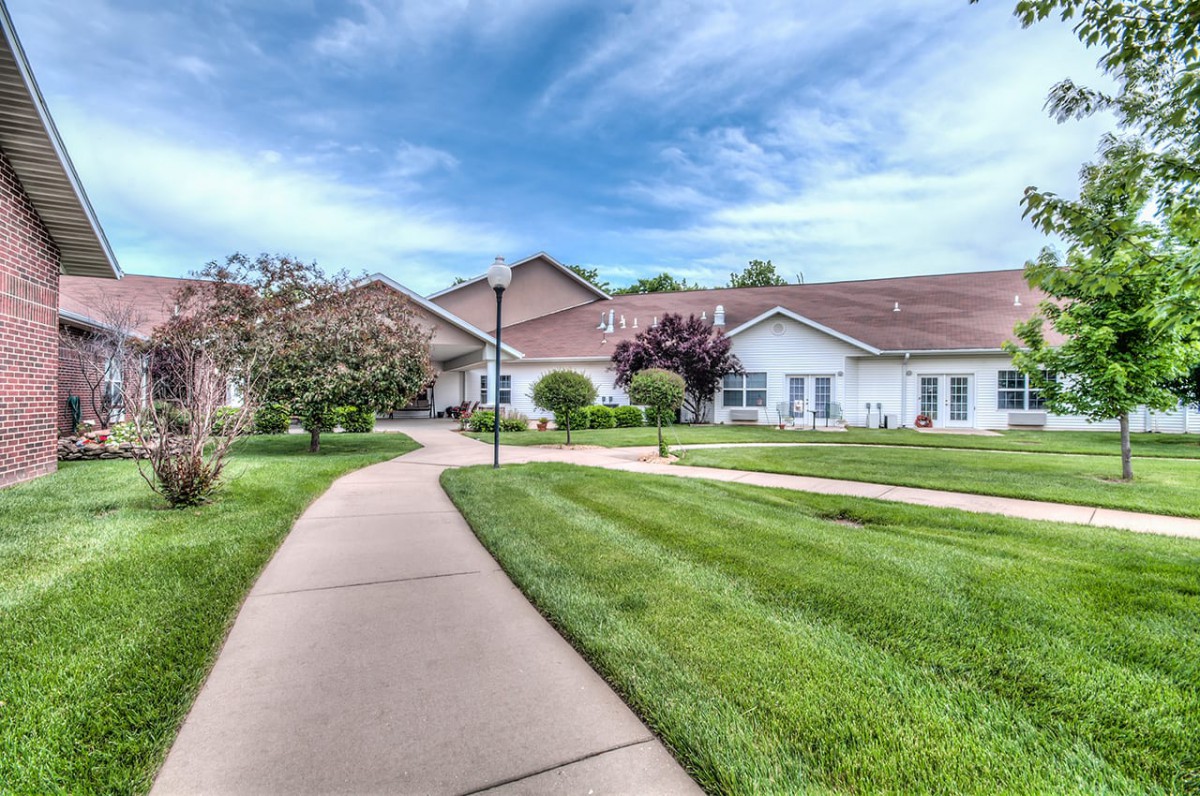 A well-maintained lawn and sidewalk lead to a residential house under a partly cloudy sky.