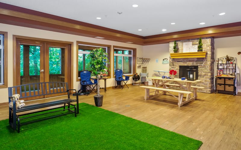 A cozy indoor room with a mix of natural and rustic elements, featuring a fireplace, wooden furniture, and artificial grass flooring.
