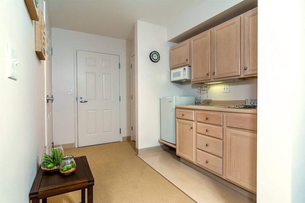 A compact apartment kitchen with light wooden cabinets and a microwave above the countertop.