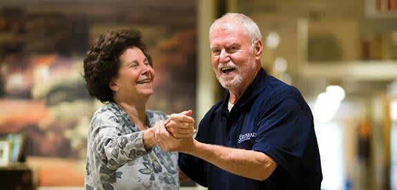 An elderly couple joyfully dancing and smiling together.
