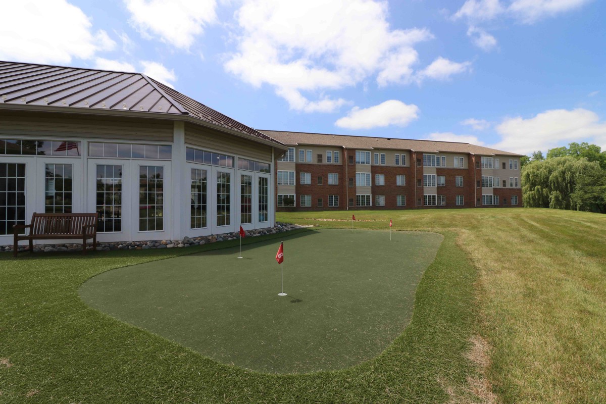 A putting green beside a building under a partly cloudy sky.