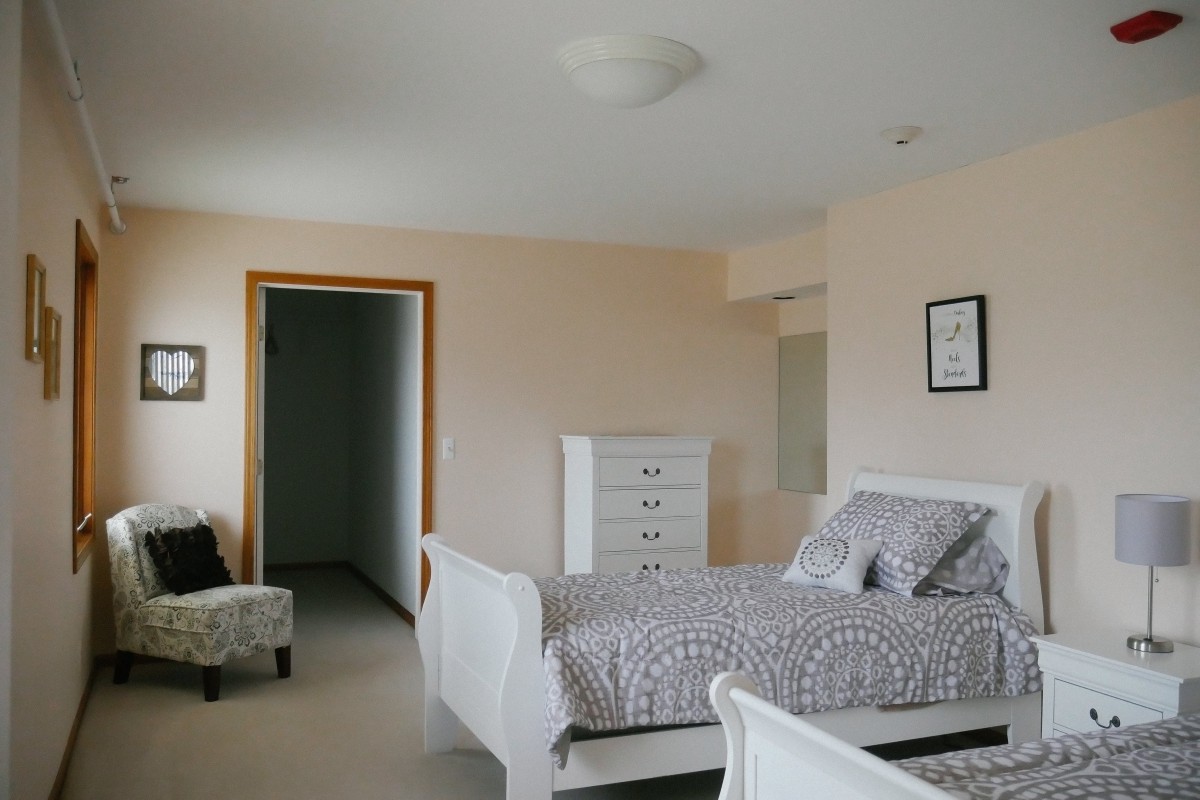 A cozy bedroom with a white bed, dresser, and patterned bedspread.