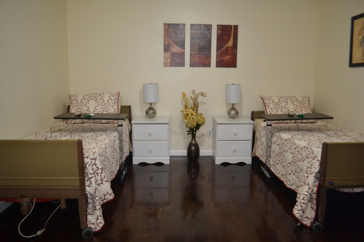 A neatly arranged bedroom with twin beds, matching nightstands, and decorative elements including lamps, a flower vase, and wall art.